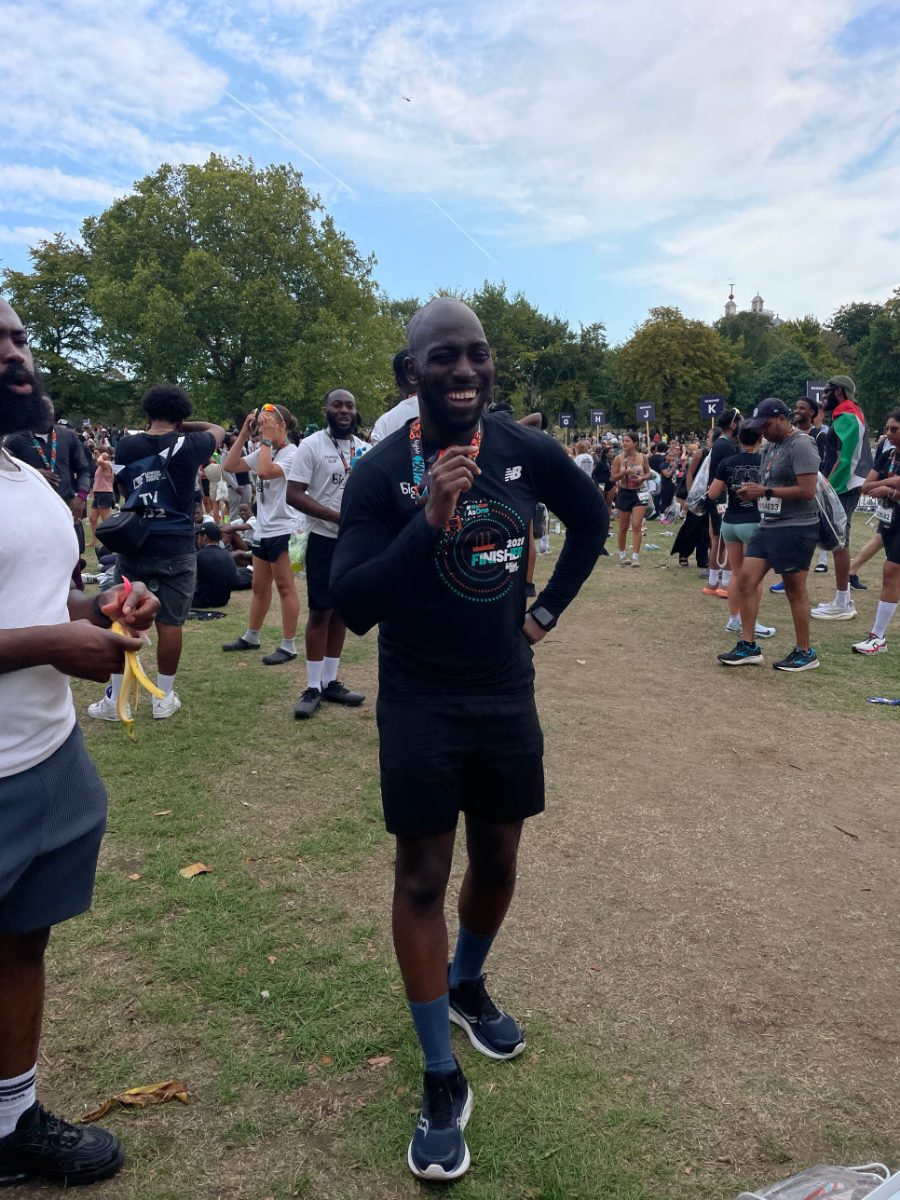 Rasheed smiling at the Big Half finish area in Greenwich Park, holding up his finisher's medal