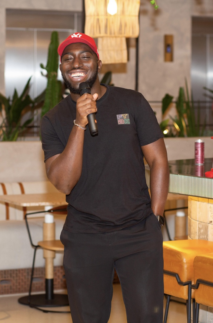 Rasheed smiling, holding a microphone and hosting an event